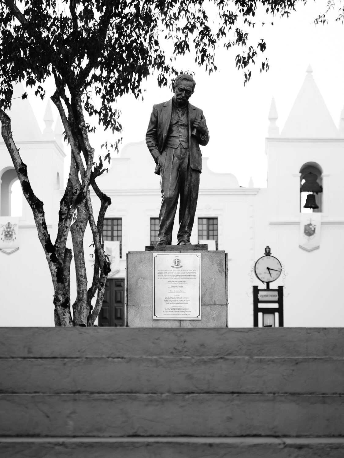 Estátua de bronze de Clóvis Beviláqua na praça com a igreja branca ao fundo.
