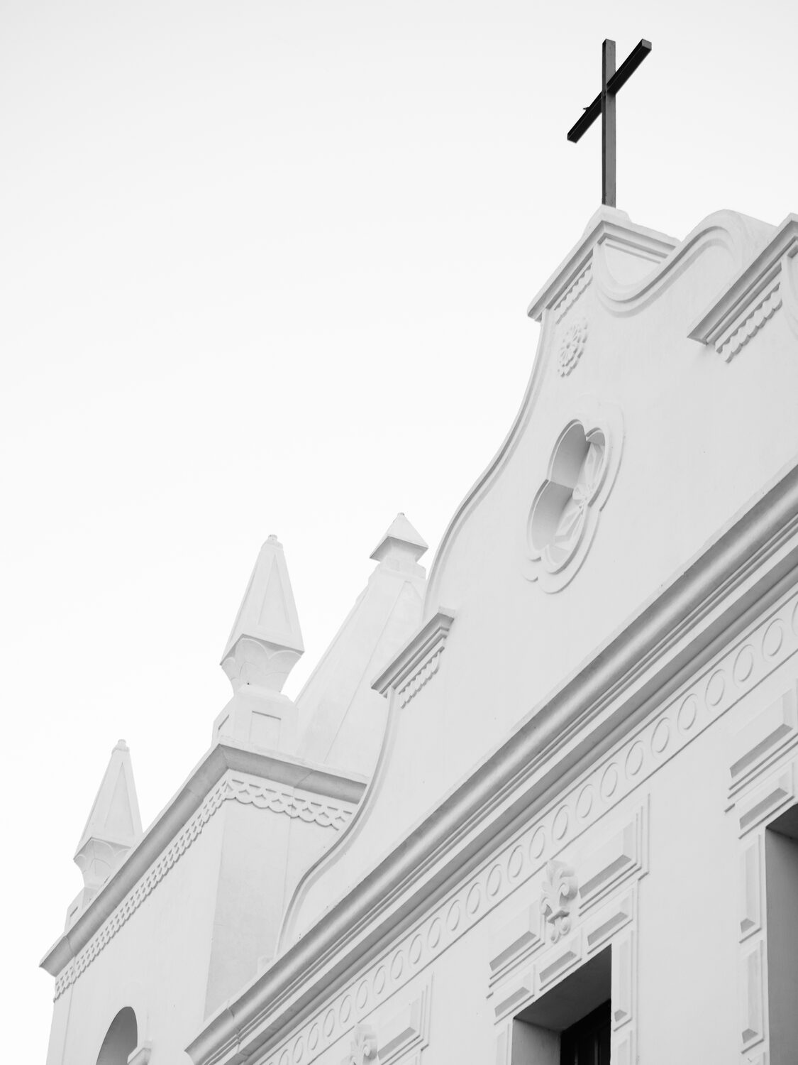 Fachada branca da igreja vista de esguelha, com pináculos e cruz.